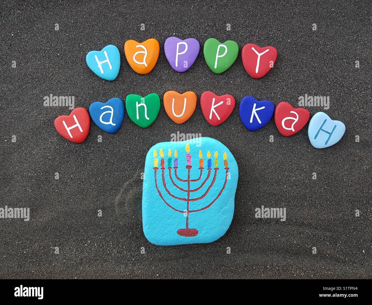 Happy Hanukkah con multicolore cuore pietre su sabbia nera vulcanica Foto Stock