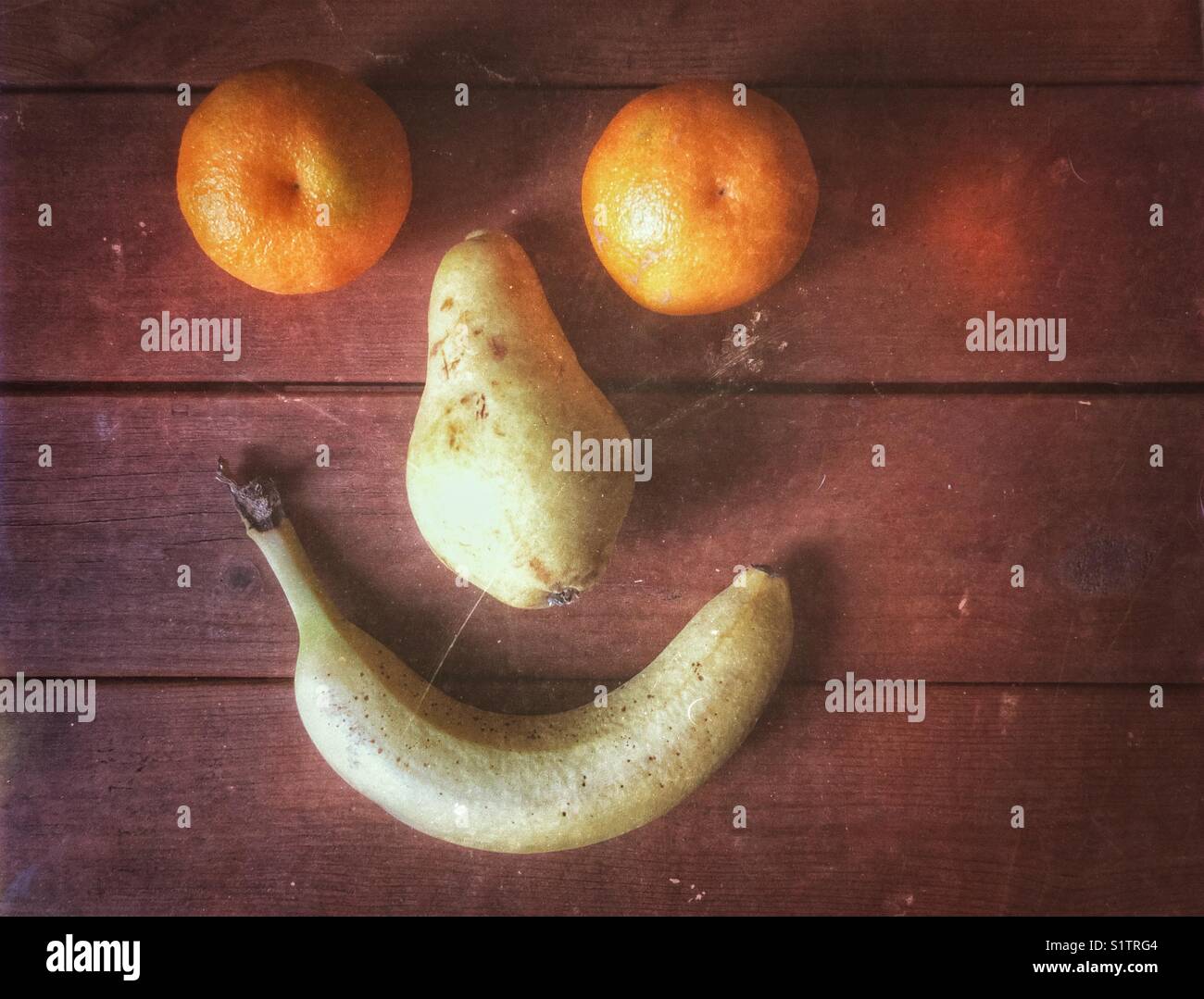 Due Arance Clementine, una pera e banana formata per fare un buon viso su assi di legno - Immagine stock catturata con smartphone