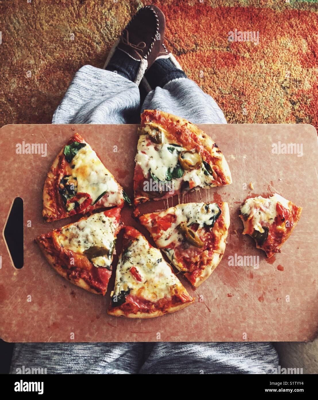 Da sopra vista di tutta la pizza con uno parzialmente mangiato slice in un bordo di taglio su una persona di giro - Immagine stock catturata con smartphone Da sopra vista di tutta la pizza con uno parzialmente mangiato slice in un bordo di taglio su una persona di giro - Immagine stock catturata con smartphone