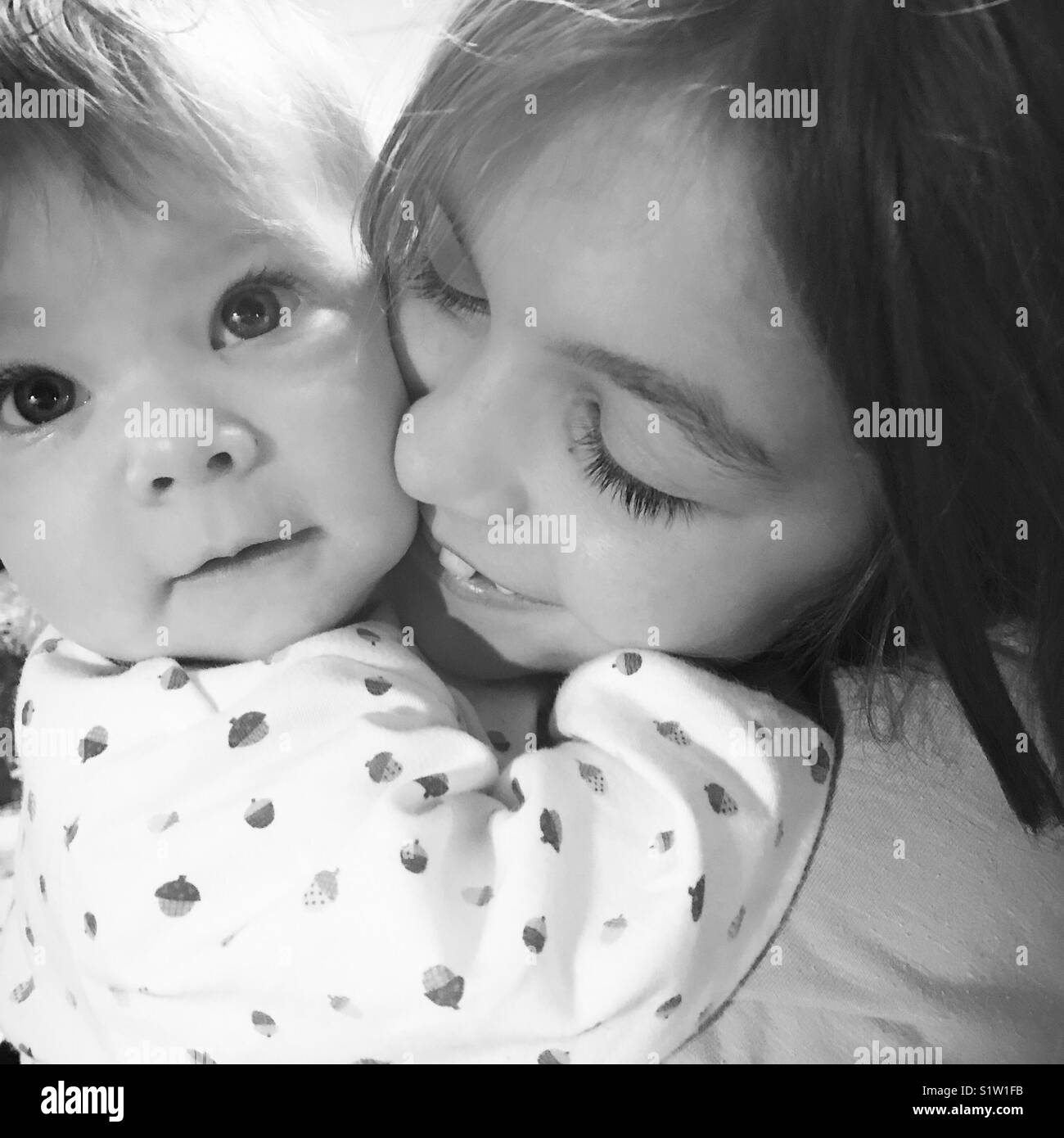 Cuddling ragazza sua sorella baby Foto Stock