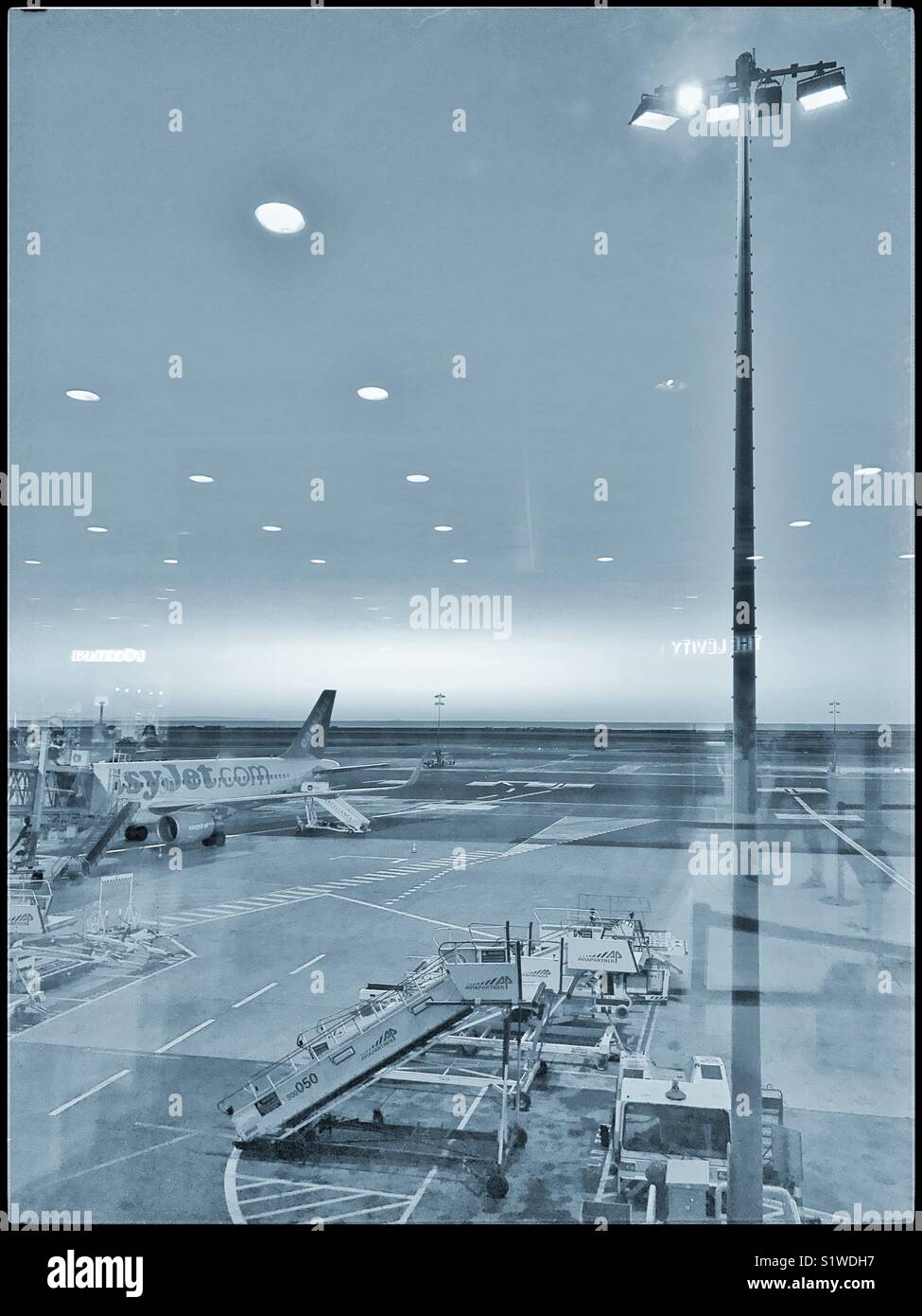 Un aeromobili EasyJet aspetta un altro volo. La vista di un aeroporto gate di partenza dalla zona di imbarco, in predawn luce. Credito foto - © COLIN HOSKINS. Foto Stock