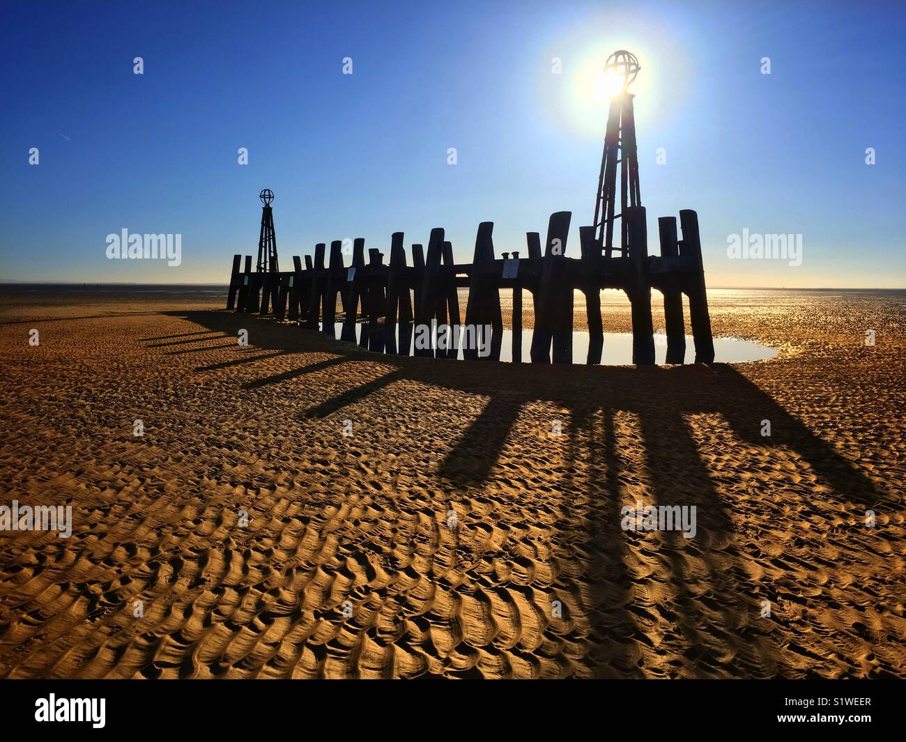 Fine abbandonati di St Annes Pier stagliano contro il sole a bassa marea Foto Stock
