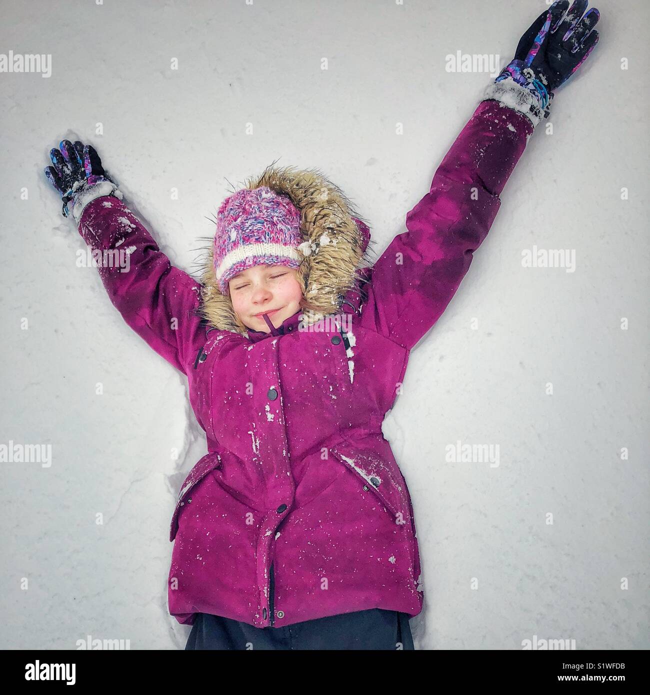 Ragazza distesa nella neve fresca con bracci fino a sorridere con gli occhi chiusi nella delizia - Immagine stock catturata con smartphone