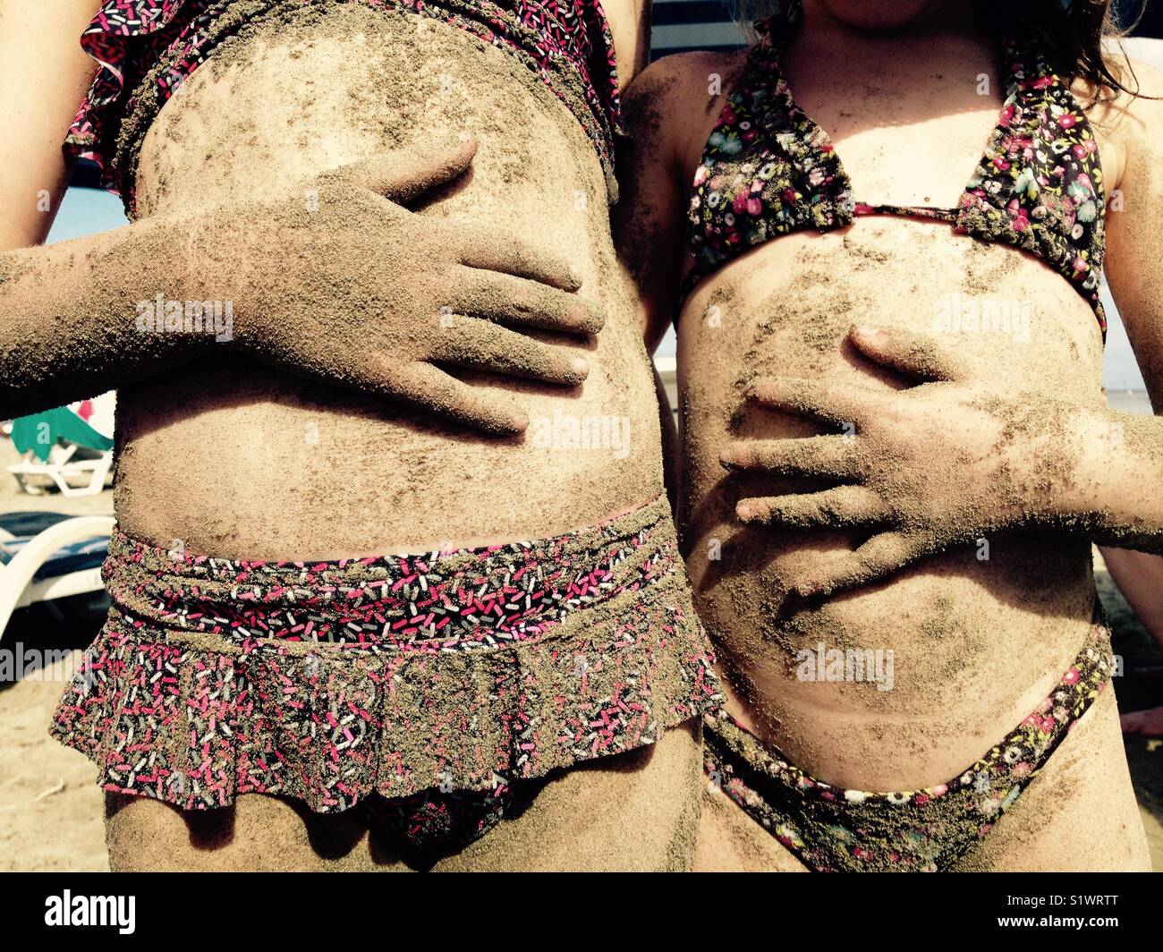Due bambini, ragazze, con sabbia di mani sul loro tummies è come se essi sono affamati, mentre presso la spiaggia. Foto Stock