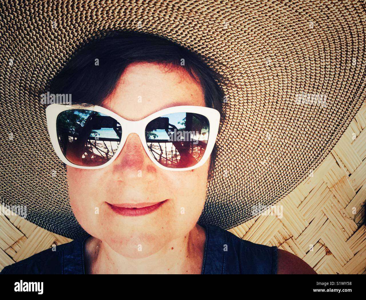 Sorridenti donna in grande cappello e 50-s bianco in stile bordati di occhiali da sole Foto Stock