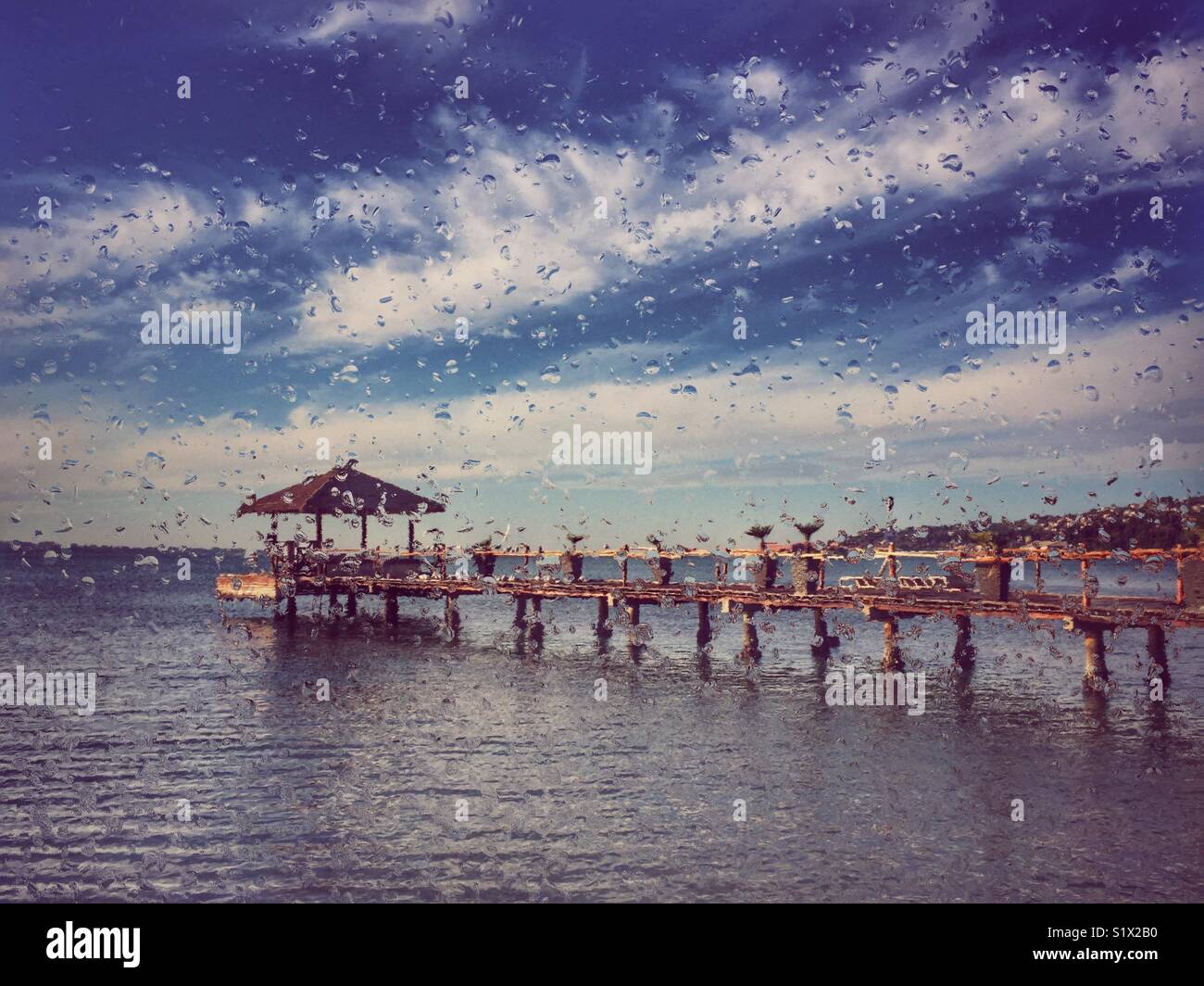Guardando attraverso una finestra con le gocce di pioggia, il beach bar sul pontile in background - Immagine stock catturata con smartphone