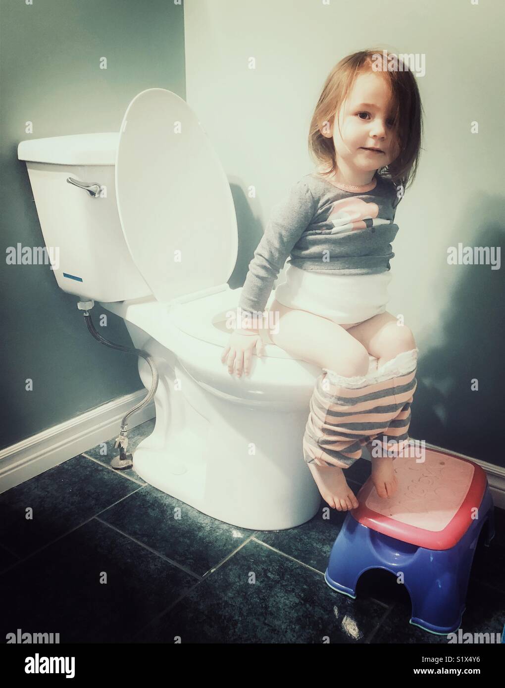 Il Toddler ragazza seduta sulla toilette in bagno con orgogliosa espressione sul viso - Immagine stock catturata con smartphone