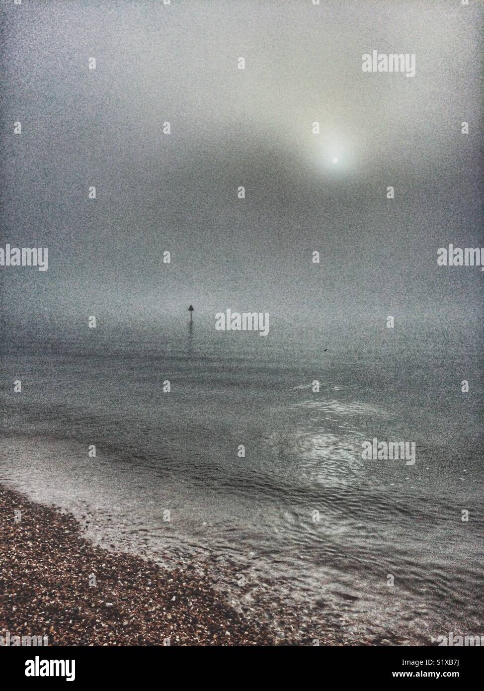Lugubre scena presso la spiaggia di rivelare il marcatore di navigazione post in acqua attraverso la nebbia. - Immagine stock catturata con smartphone