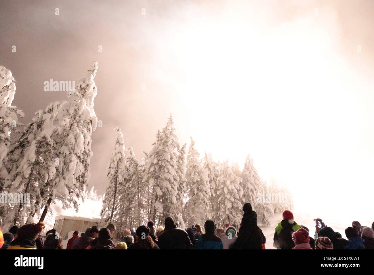 Una folla guarda un accecamento fuochi d' artificio esplodono su una montagna innevata. - Immagine stock catturata con smartphone