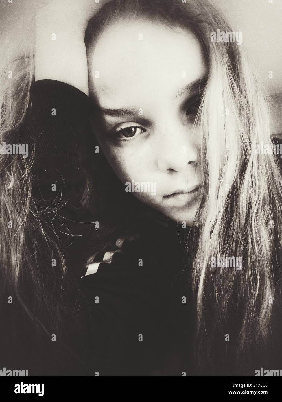 Creative ritratto monocromatica di una ragazza con la mano sulla testa guardando la fotocamera con capelli lunghi che coprono parzialmente la faccia - Immagine stock catturata con smartphone