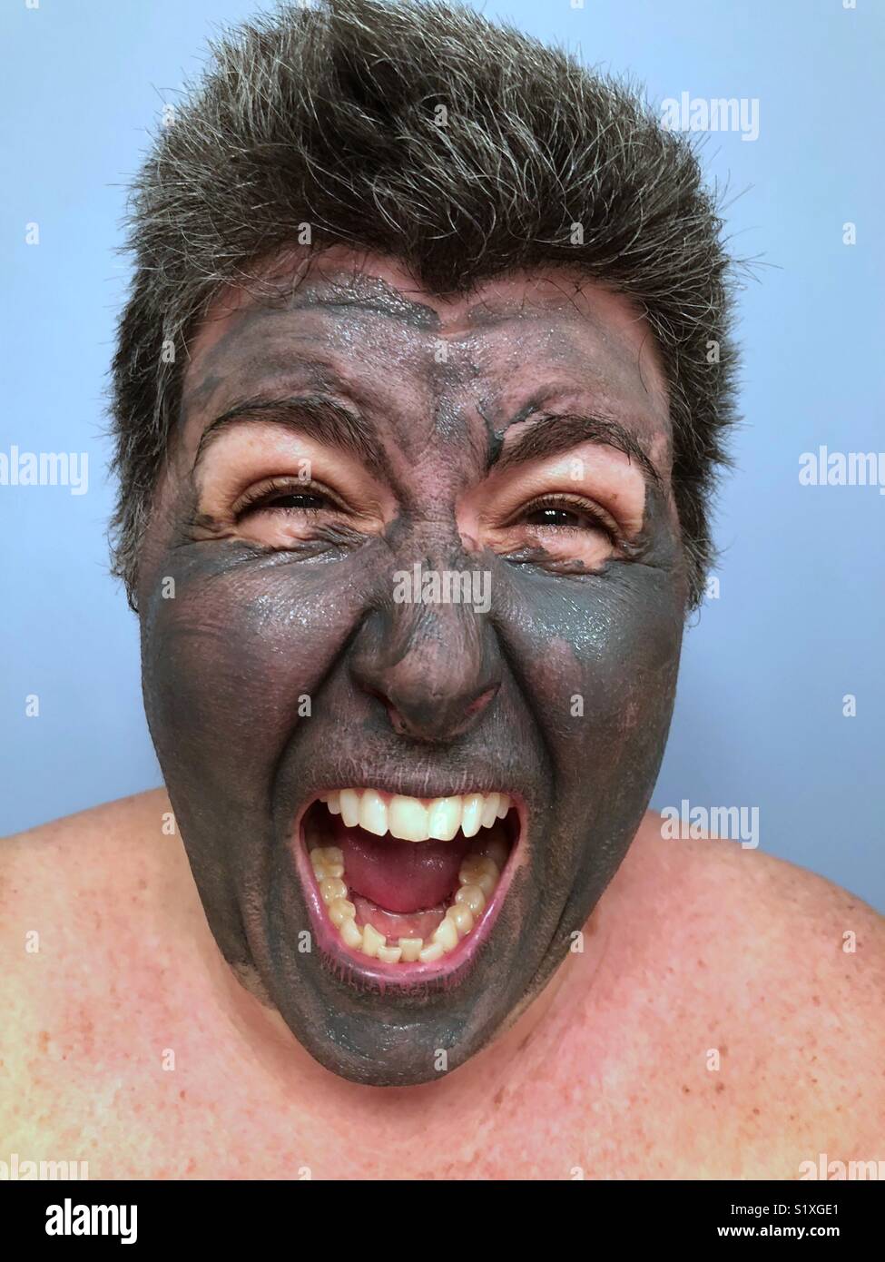 Un primo piano ritratto di una donna caucasica facendo una estrema faccia ridere con la bocca aperta indossando un carbone maschera di fango Foto Stock