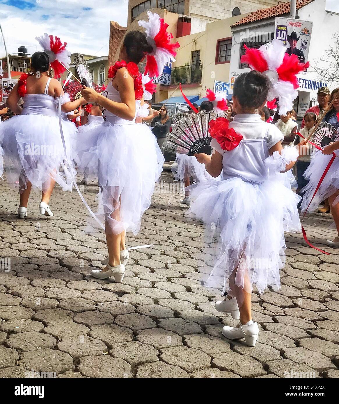 La vista posteriore di un gruppo di ballo di ragazze di varie età vestita di bianco e rosso bellissimi costumi che passano da durante il Mardi Gras Carnaval parade di Chapala, Messico. Foto Stock