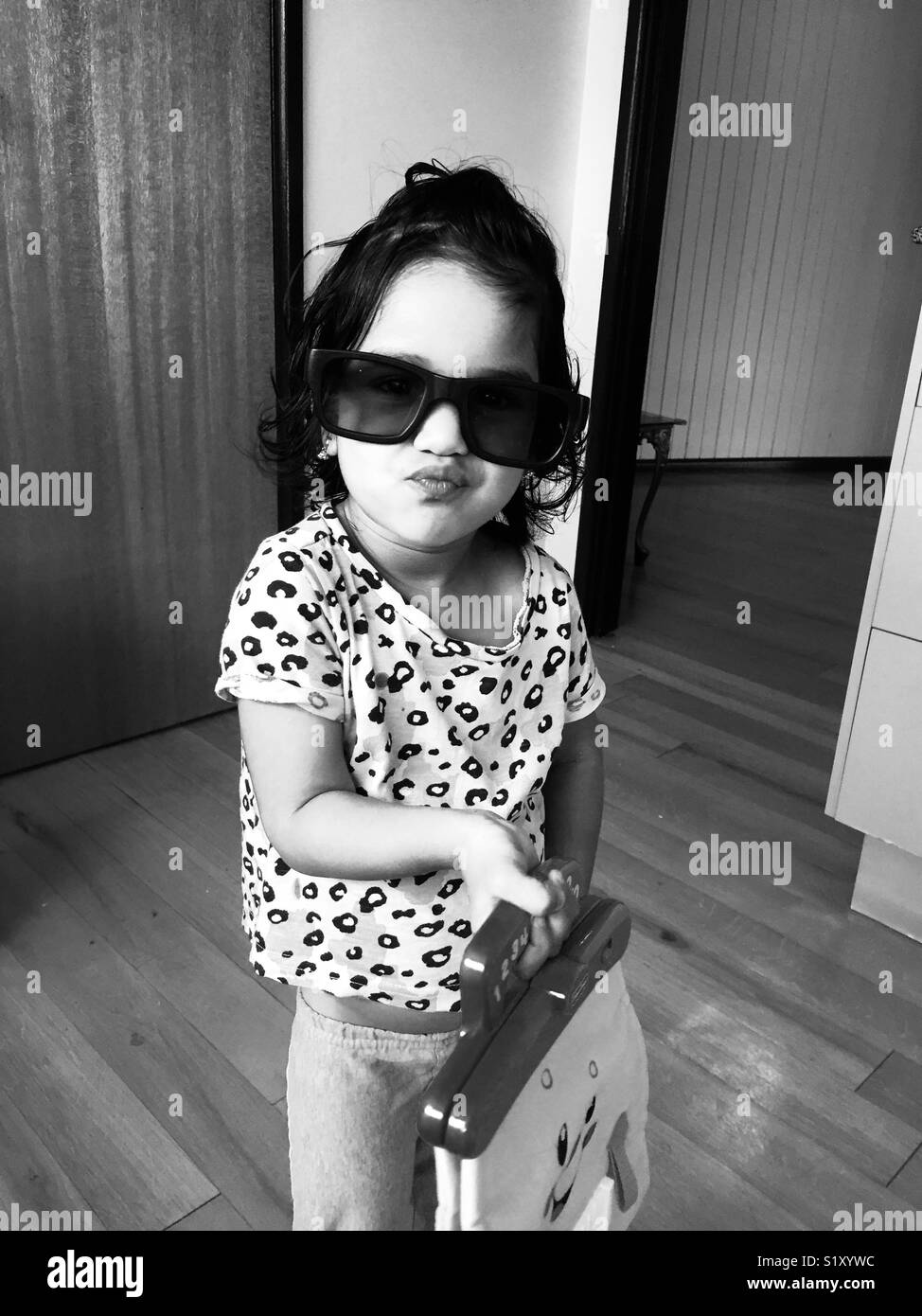 Una bambina di tre anni finge di andare a fare shopping con grandi occhiali e un giocattolo di frizione. Foto Stock