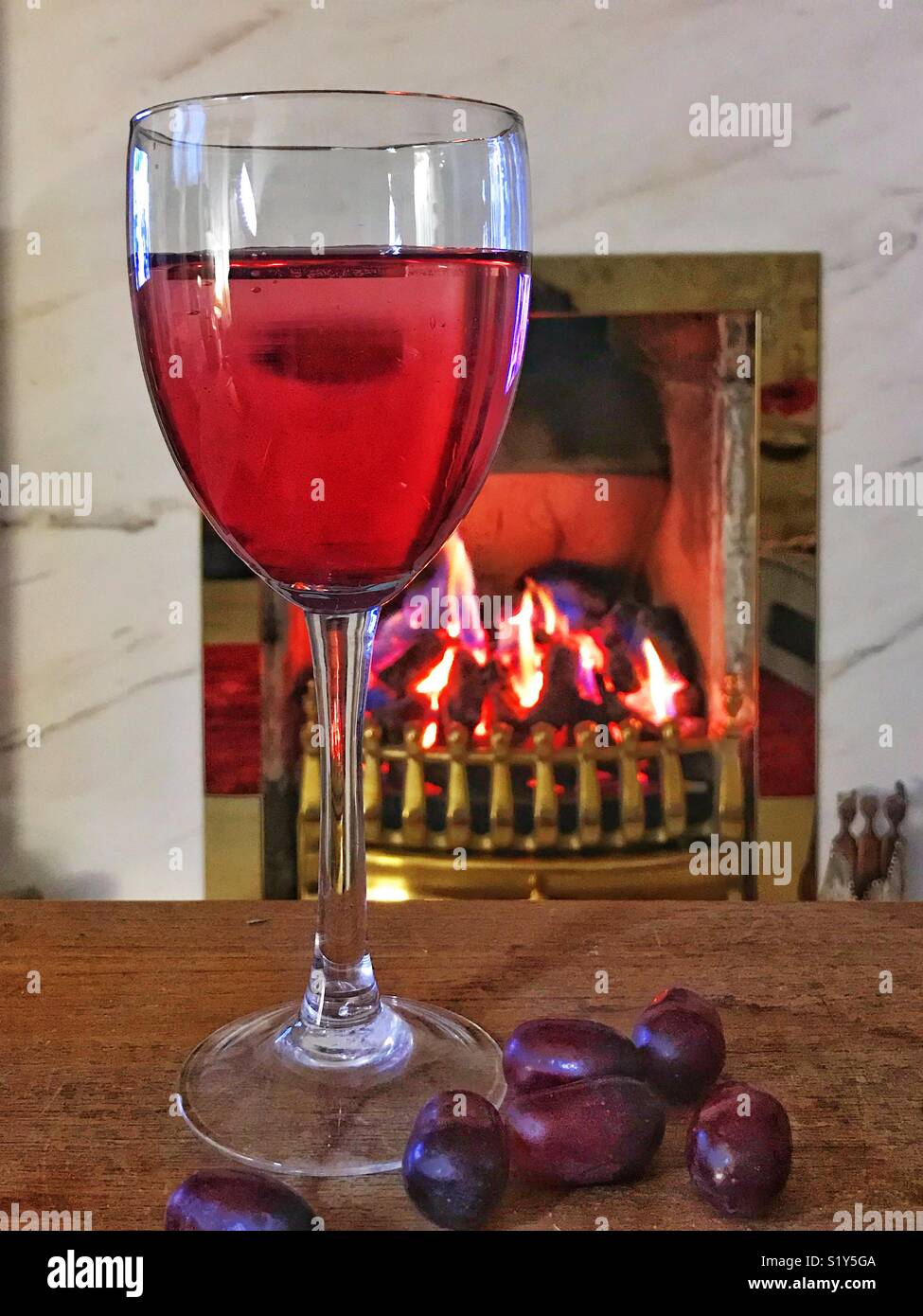 Ancora la vita di un bicchiere di vino rosso e uva rossa su un tavolo di legno davanti ad un fuoco di carbone con ottone circonda Foto Stock