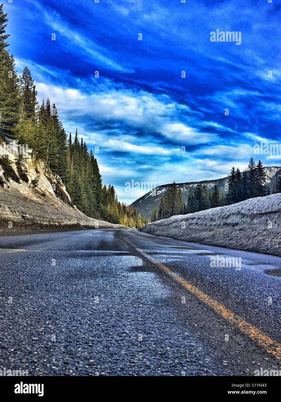 Un vuoto di autostrada conduce lontano tra gli alberi e le montagne nel sud della British Columbia, Canada su un bellissimo fine giornata invernale. Linea Snowbanks la strada. Foto Stock