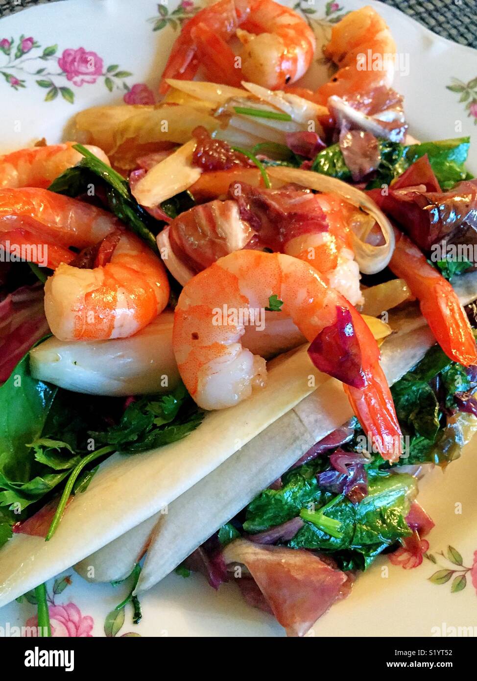 Gamberi saltati su un letto di foglie di indivia e spinaci servito su una piastra di cina Foto Stock