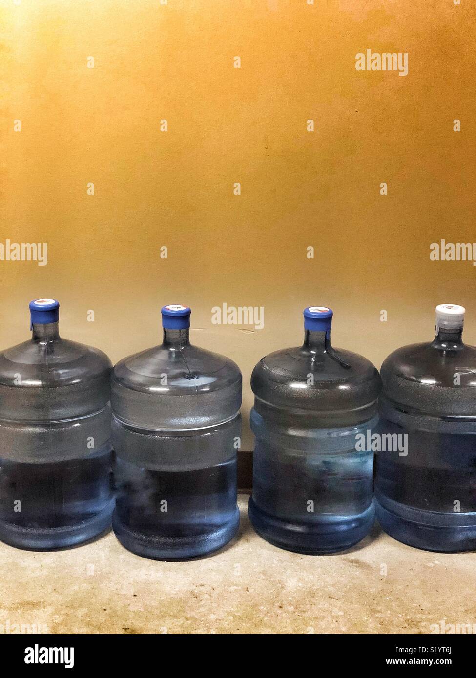 Fila di brocche di plastica dell'acqua contro una parete piana - Immagine stock catturata con smartphone