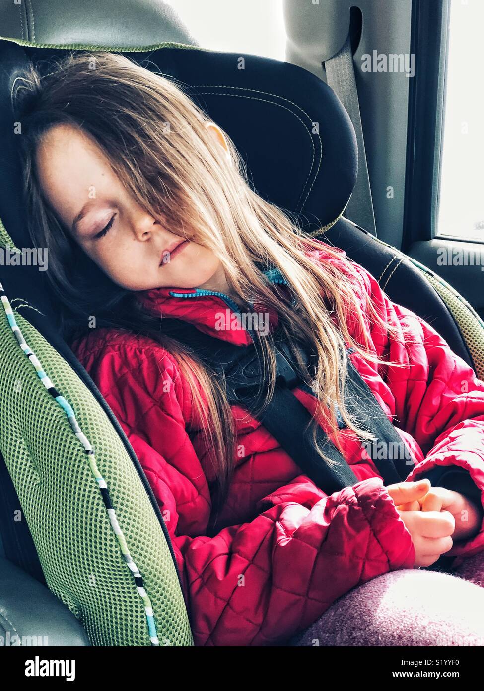 5 anno vecchia ragazza dorme in rivolta in avanti il sedile auto con imbracatura a 5 punti e capelli lunghi che coprono la metà il suo volto Foto Stock