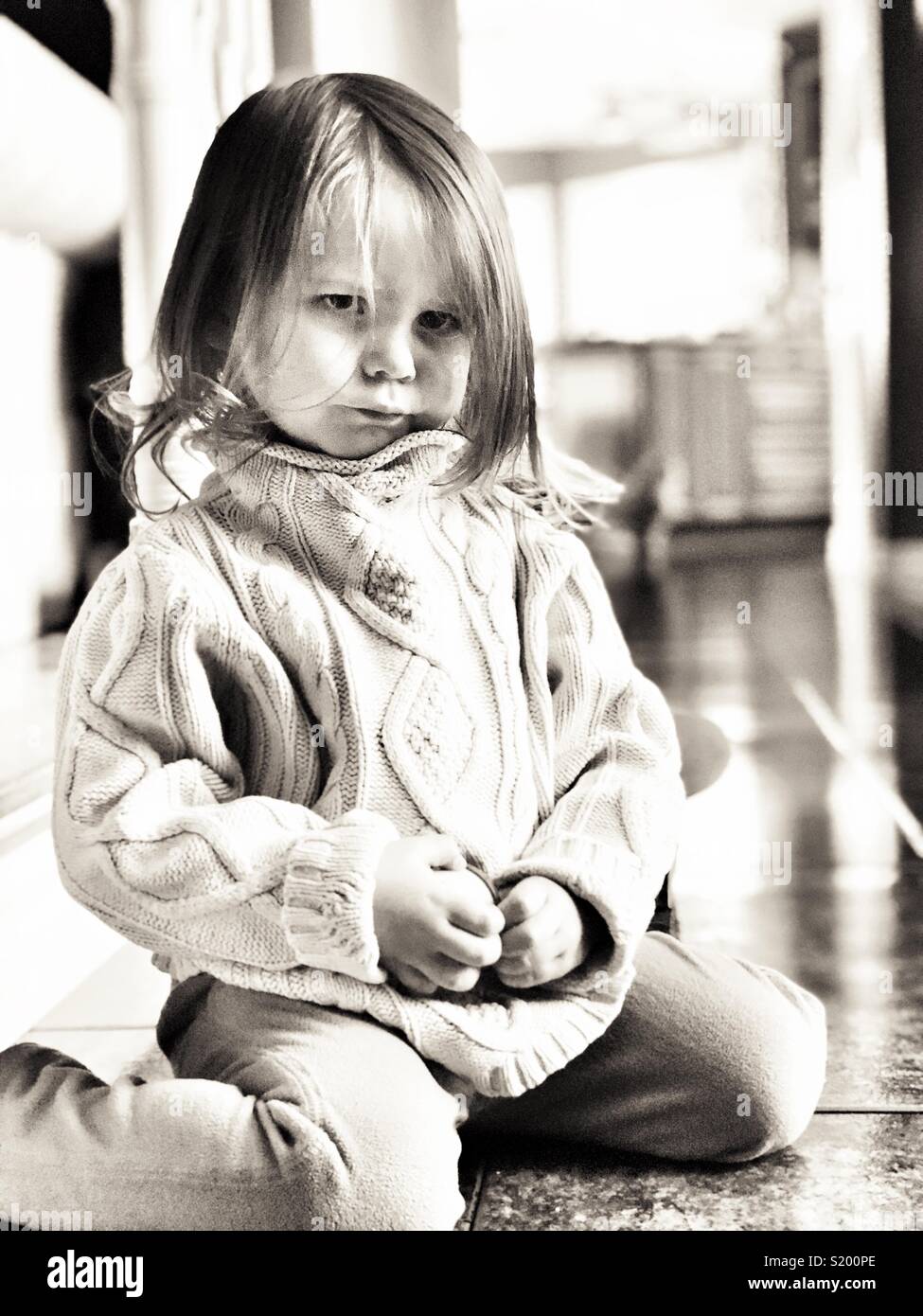 Immagine in bianco e nero di toddler cerca ragazza triste e arrabbiato sul pavimento di piastrelle con retroilluminazione brillante - Immagine stock catturata con smartphone