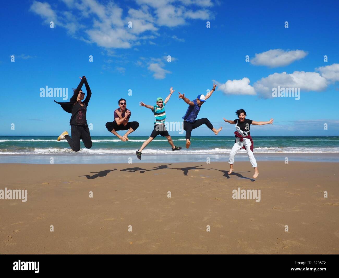 Amici divertirsi saltando su una spiaggia in una giornata di sole Foto Stock