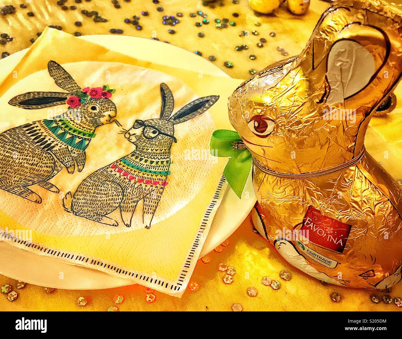 Il cioccolato coniglietto di pasqua avvolti in lamina d'oro di peering della carta verso il basso un tovagliolo di carta con due conigli di Pasqua - Immagine stock catturata con smartphone