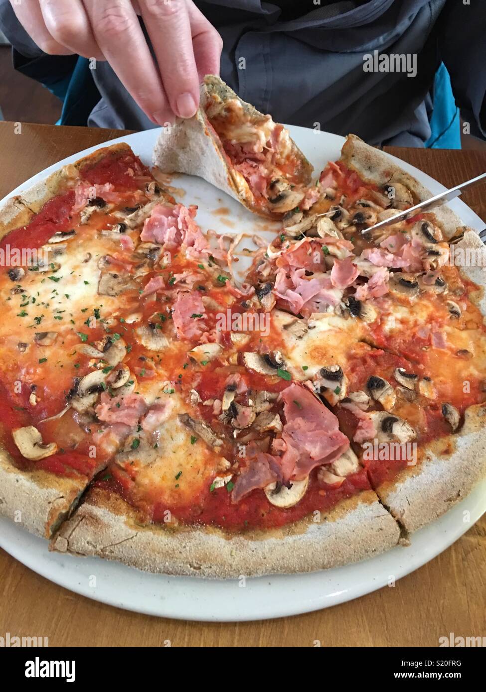 Uomo di mangiare un prosciutto e funghi senza glutine pizza fatta con una base di canapa crosta - Immagine stock catturata con smartphone