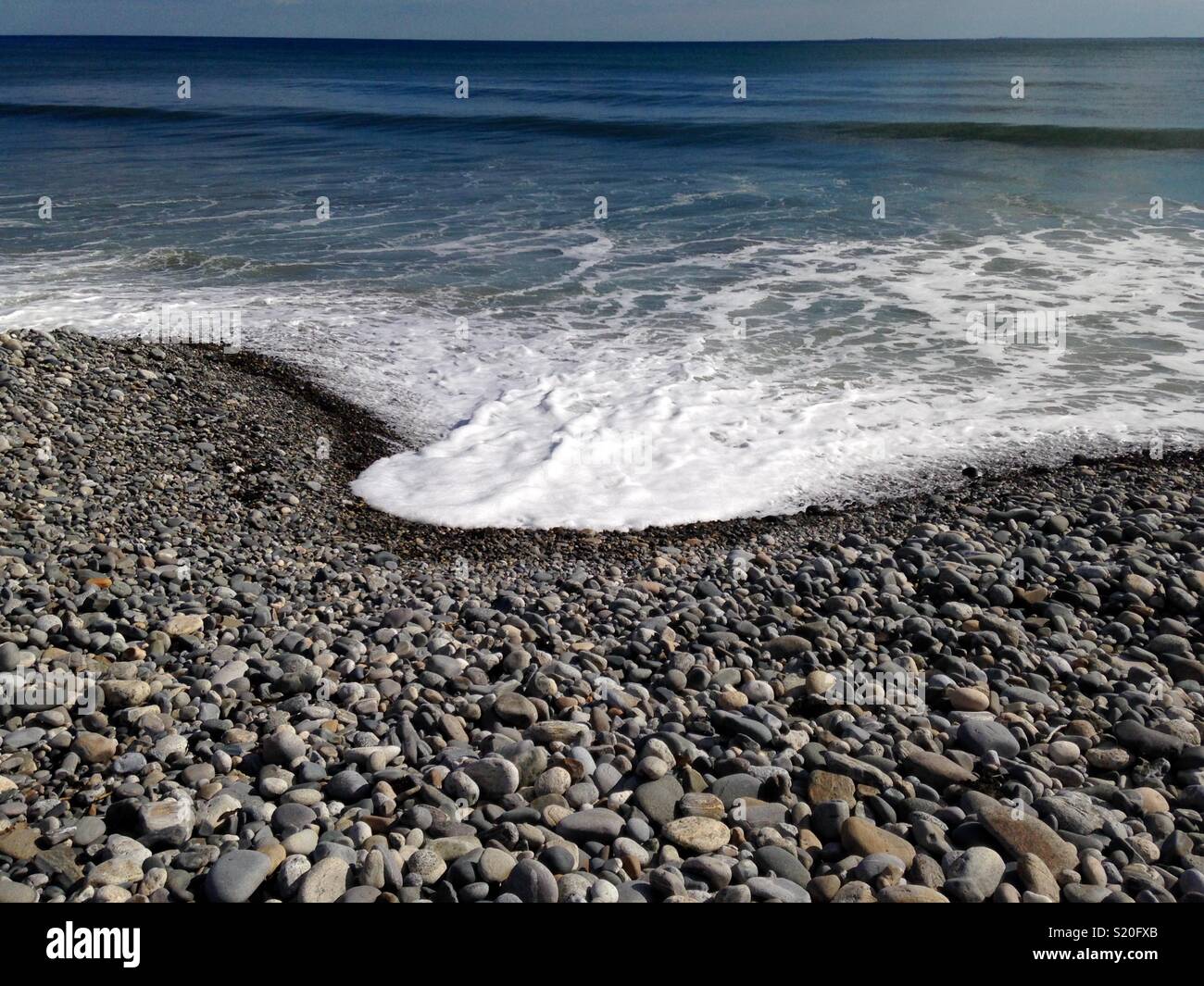 Vorticoso di schiuma di mare e di onde che si infrangono sugli scogli lungo la riva Foto Stock
