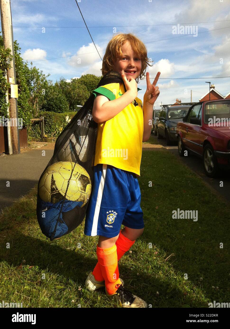 Giovane ragazzo in kit calcio con la sacca di sfere sul modo di formazione di calcio Foto Stock