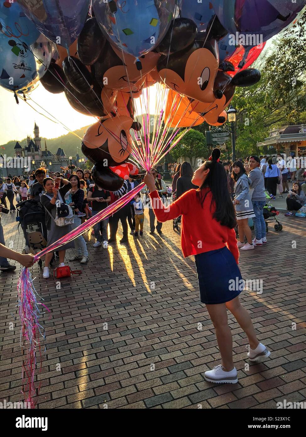 Un turista in posa per una fotografia con un mazzetto di Mickey Mouse-palloncini a tema Disneyland, Hong Kong - Immagine stock catturata con smartphone