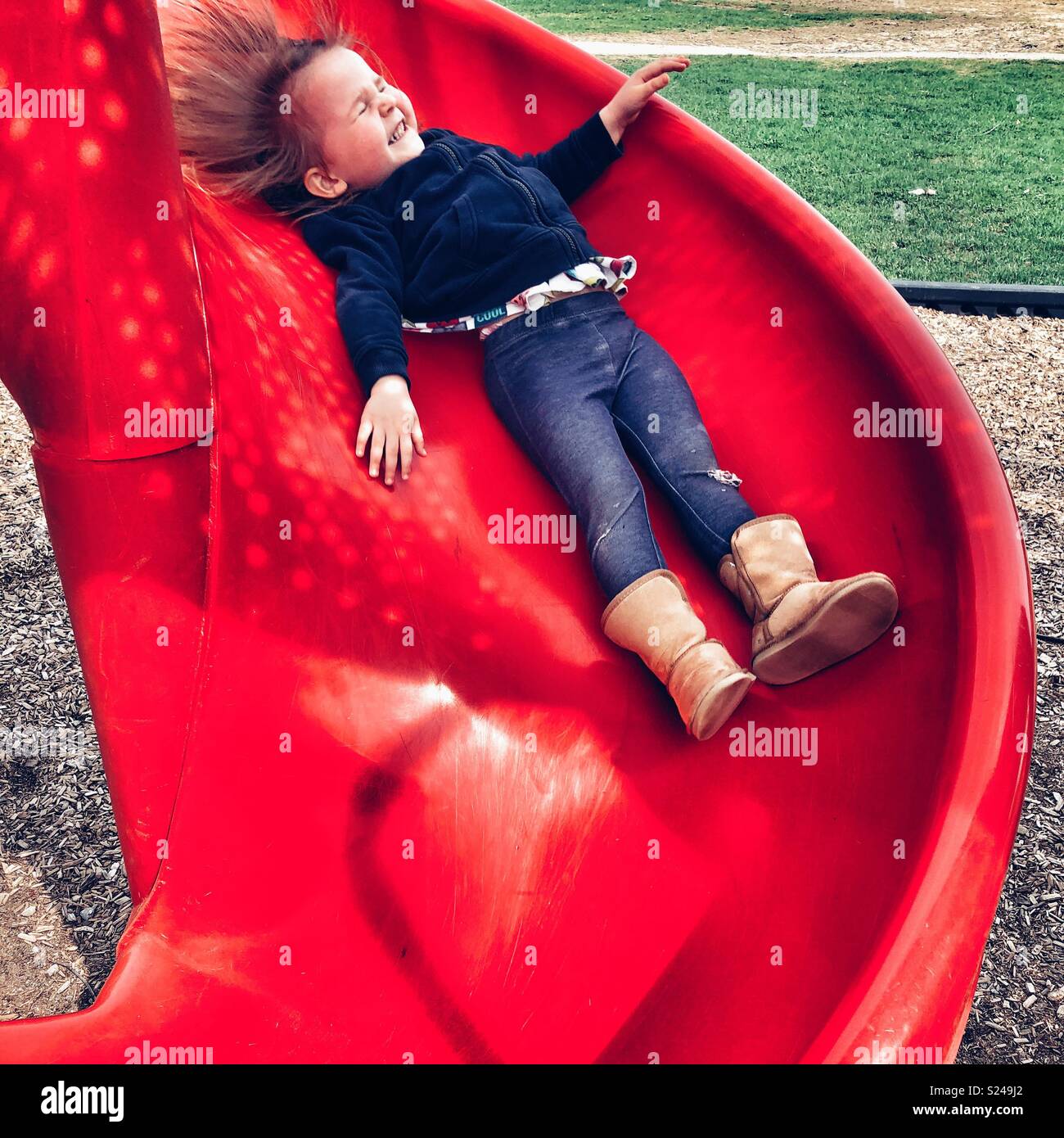 Il Toddler ragazza sorridente felicemente mentre lo scorrimento verso il basso un parco giochi rosso slitta Foto Stock