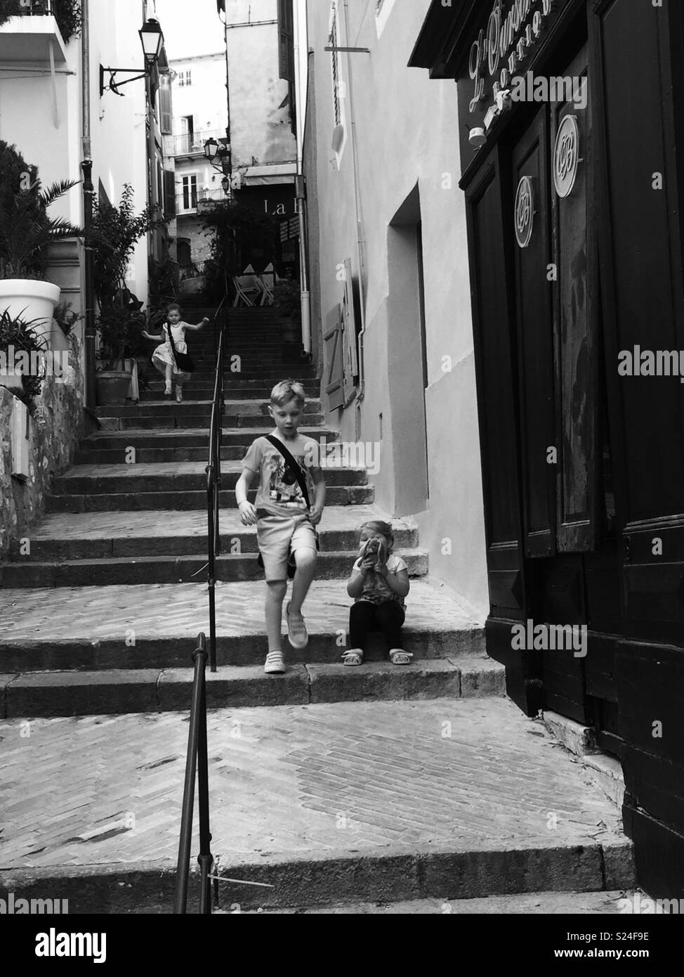 I bambini correndo giù alcuni passi su una strada laterale nel sud della Francia di essere guardato dalla loro piccola sorella sat li guarda volare oltre. Foto Stock