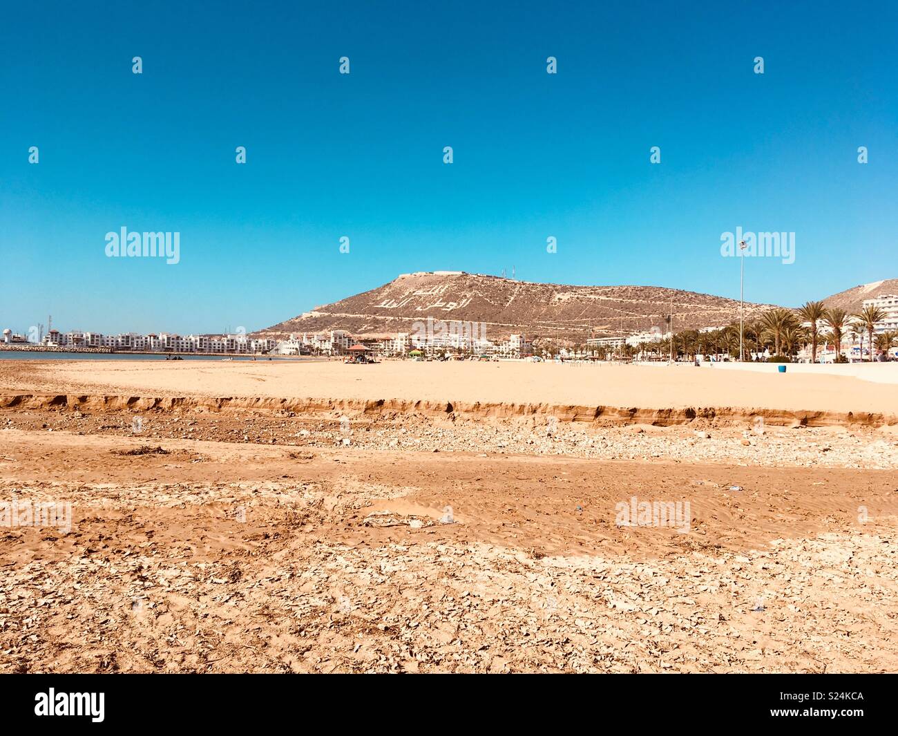 Una collina con scrittura araba dietro di sabbia dorata, alberghi e appartamenti presso la spiaggia di Agadir, Marocco Foto Stock