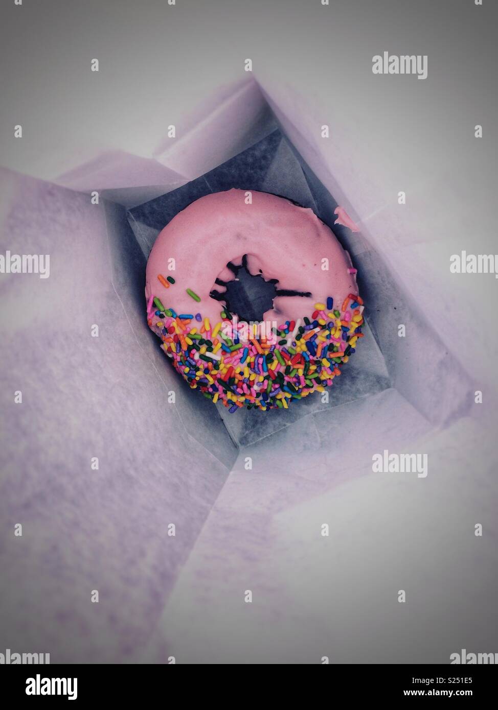 Una rosa torta smerigliato ciambella con spruzzino nel fondo di un libro bianco in borsa - Immagine stock catturata con smartphone