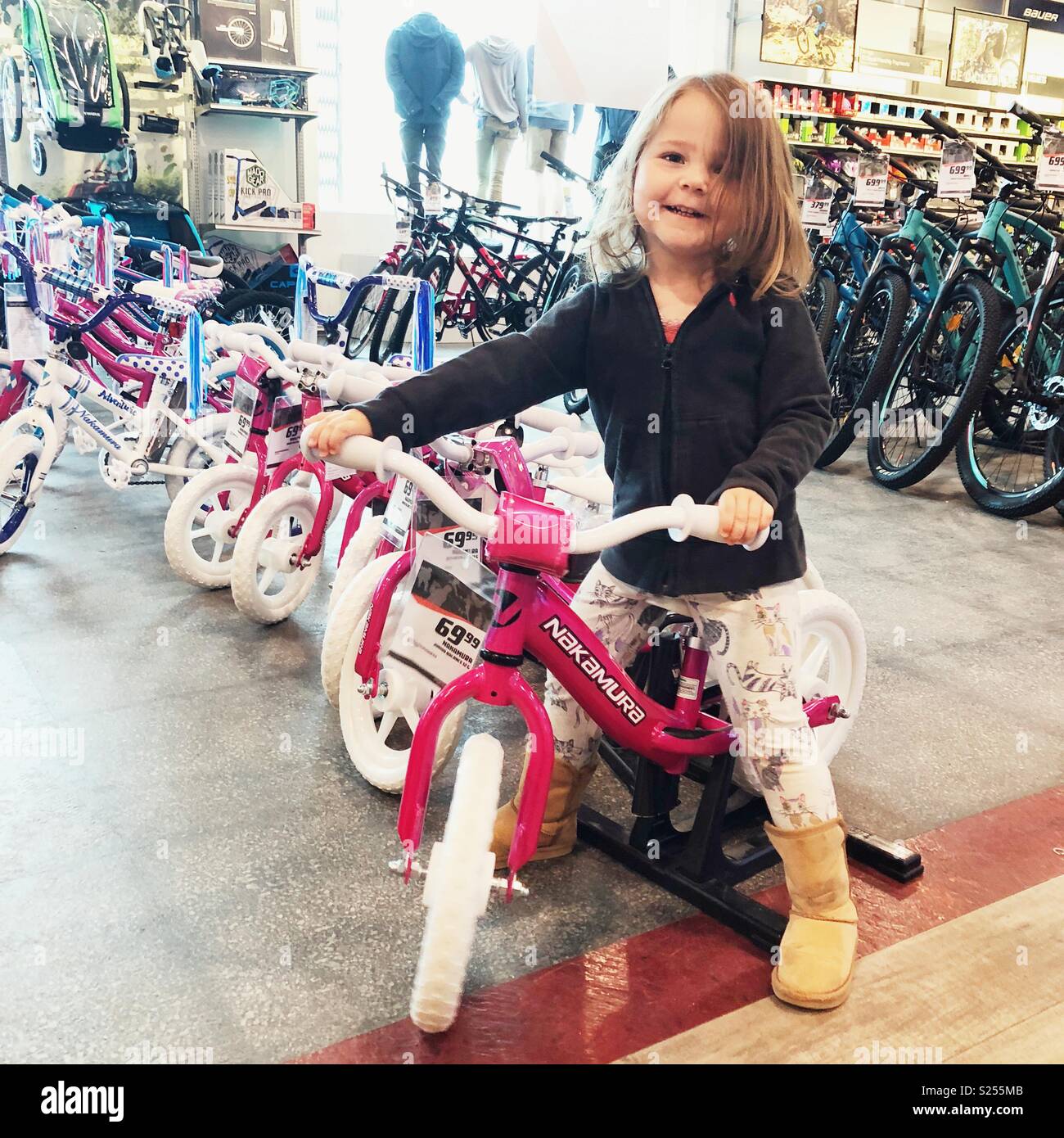 Il Toddler ragazza seduta a spingere la bicicletta in un negozio di biciclette - Immagine stock catturata con smartphone