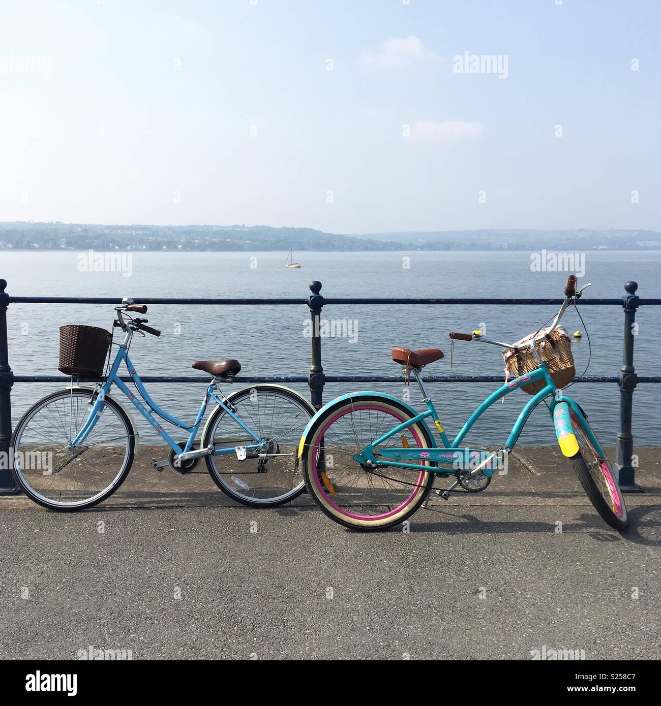 Due biciclette colorate contro le ringhiere sul lungomare di Mumbles, Swansea, Galles del Sud Foto Stock