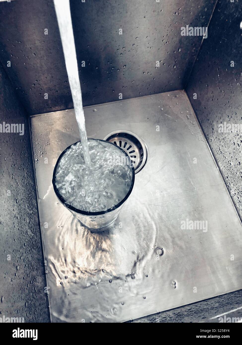 Acqua di rubinetto di riempimento e la fuoriuscita di un vetro di grandi dimensioni in un lavello in acciaio inox Foto Stock