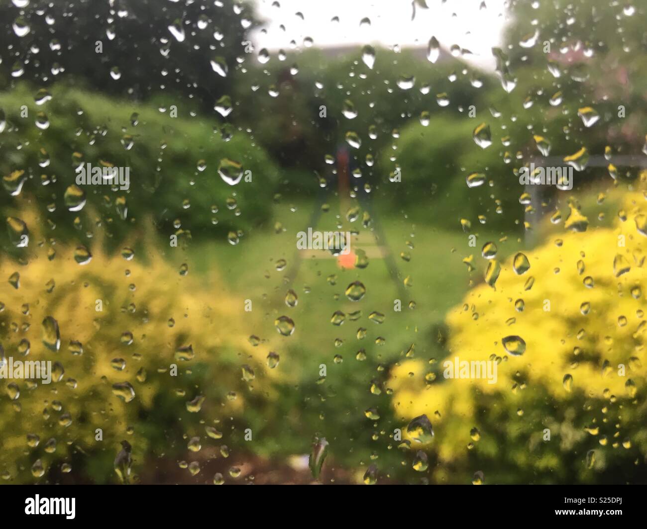 Gocce di pioggia su una finestra che guarda ad un giardino con un bambino visibile di oscillazione. Foto Stock