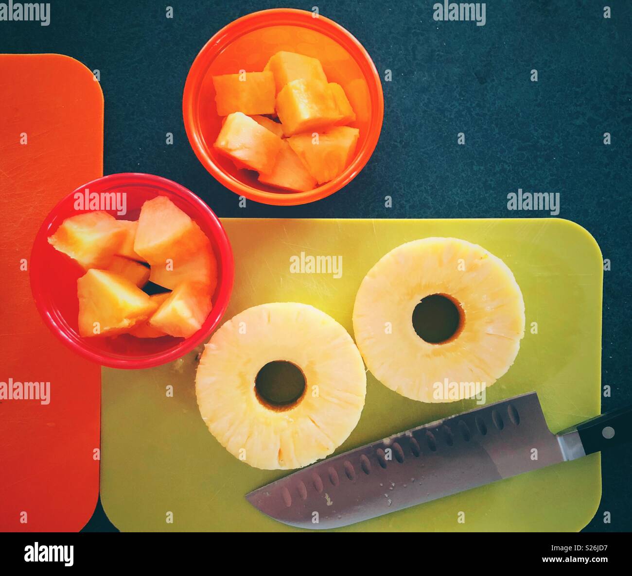 Fette di ananas e pezzetti sul verde e arancione schede di taglio con il coltello e i contenitori in plastica Foto Stock