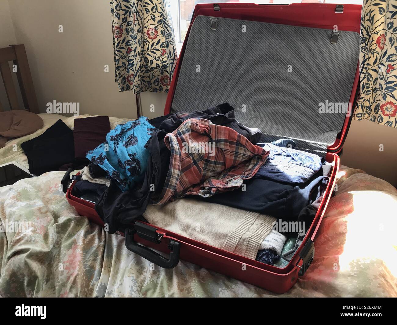 Big Red in valigia su un letto pieno di vestiti Foto Stock