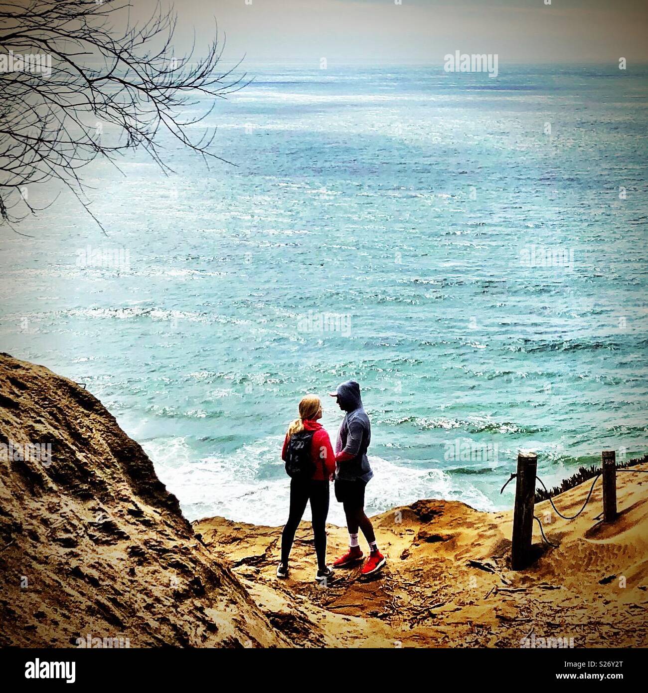 Romantico coppia giovane, uomo e donna, guardando in ogni occhi dell'altro in cima golden California scogliere che si affaccia sul bellissimo Oceano Pacifico che riflette il sole estivo - Immagine stock catturata con smartphone