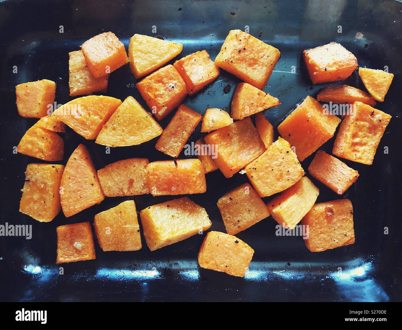 Forno arrosto e condite la zucca tagliata a cubetti in un vetro piatto da forno Foto Stock