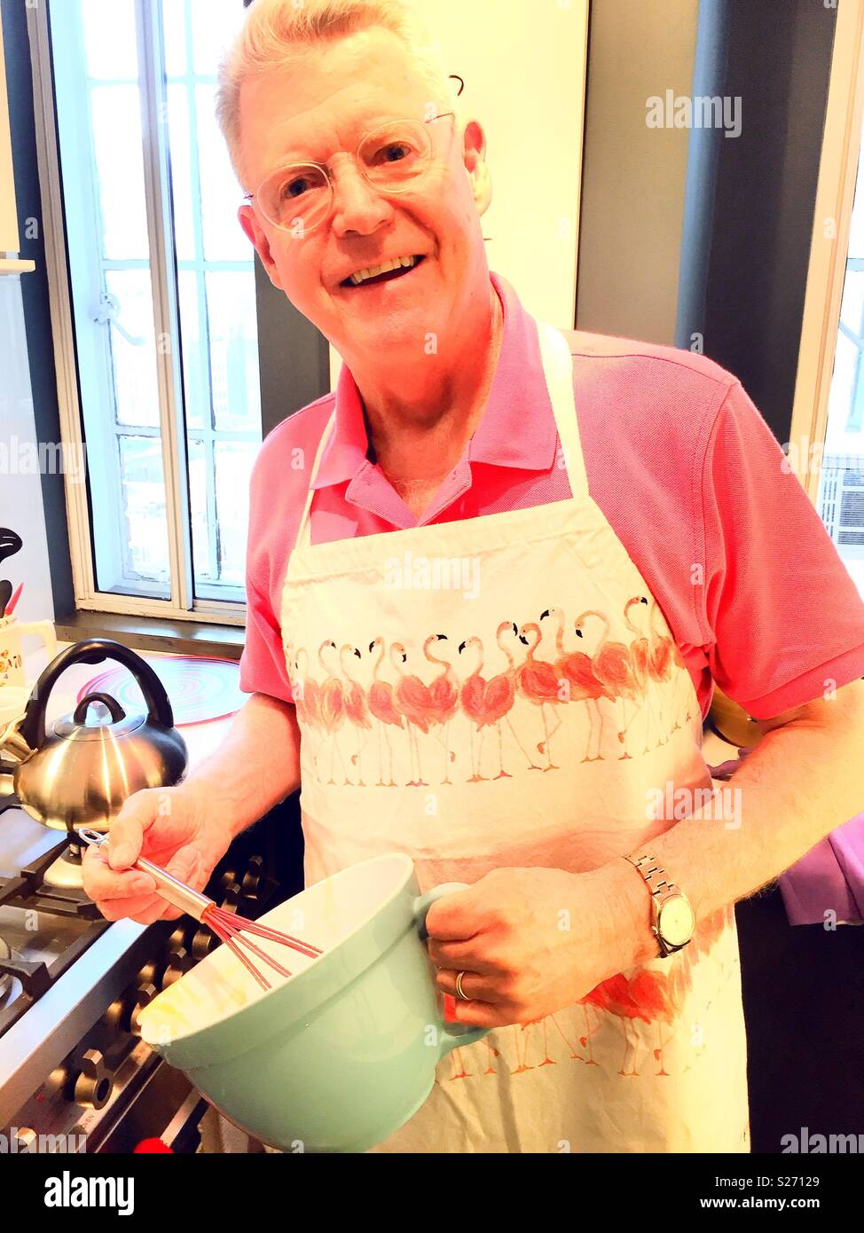 Senior uomo in appartamento cucina brillantemente vestito con grembiule flamingo, STATI UNITI D'AMERICA - Immagine stock catturata con smartphone