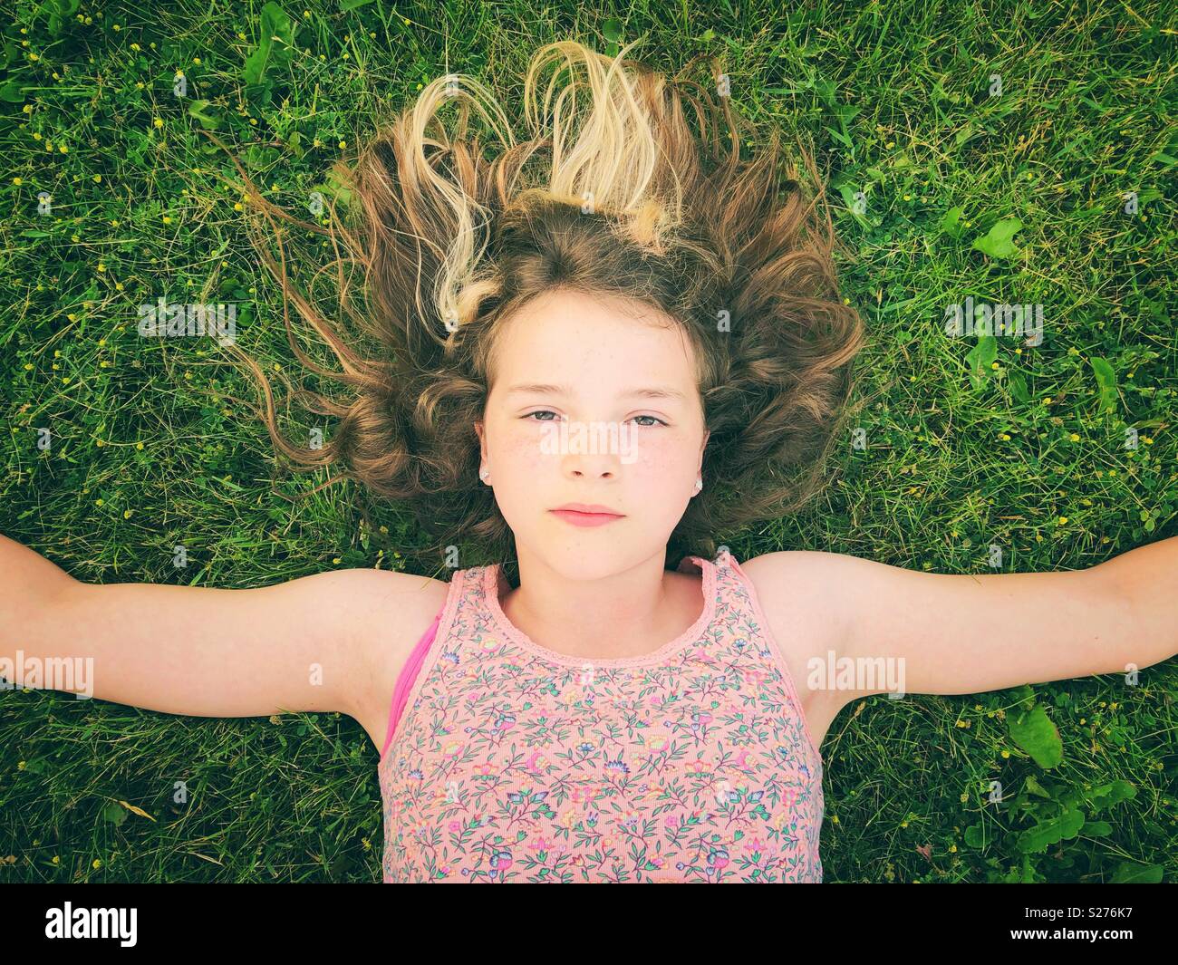 11 anno vecchia ragazza posa in erba con braccia e espressione seria sul suo viso Foto Stock