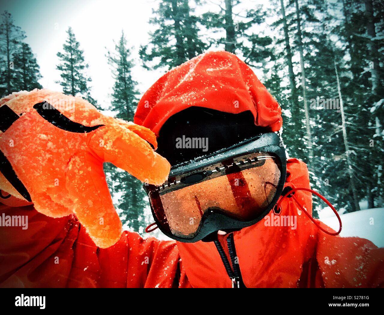 Snowboarder in arancione la neve marcia, guanti e maschera di innumerevoli gesti di pace in mezzo a una bufera di neve di montagna - Immagine stock catturata con smartphone