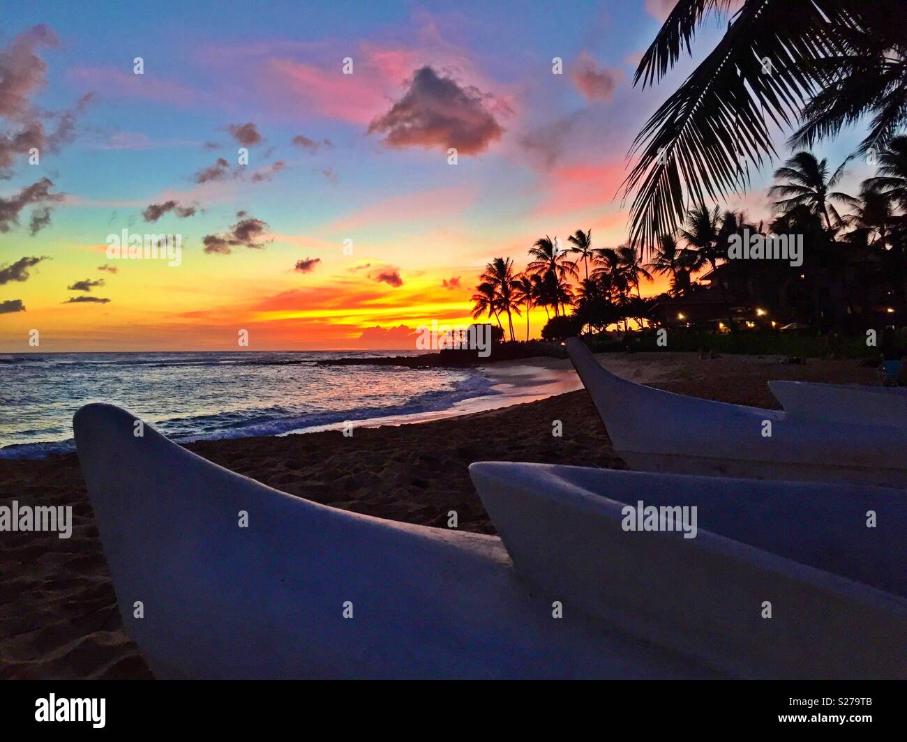 Canoe Outrigger spiaggiata per il giorno come il sole tramonta sul bellissimo tropicale oceano Pacifico nelle Hawaii - Immagine stock catturata con smartphone