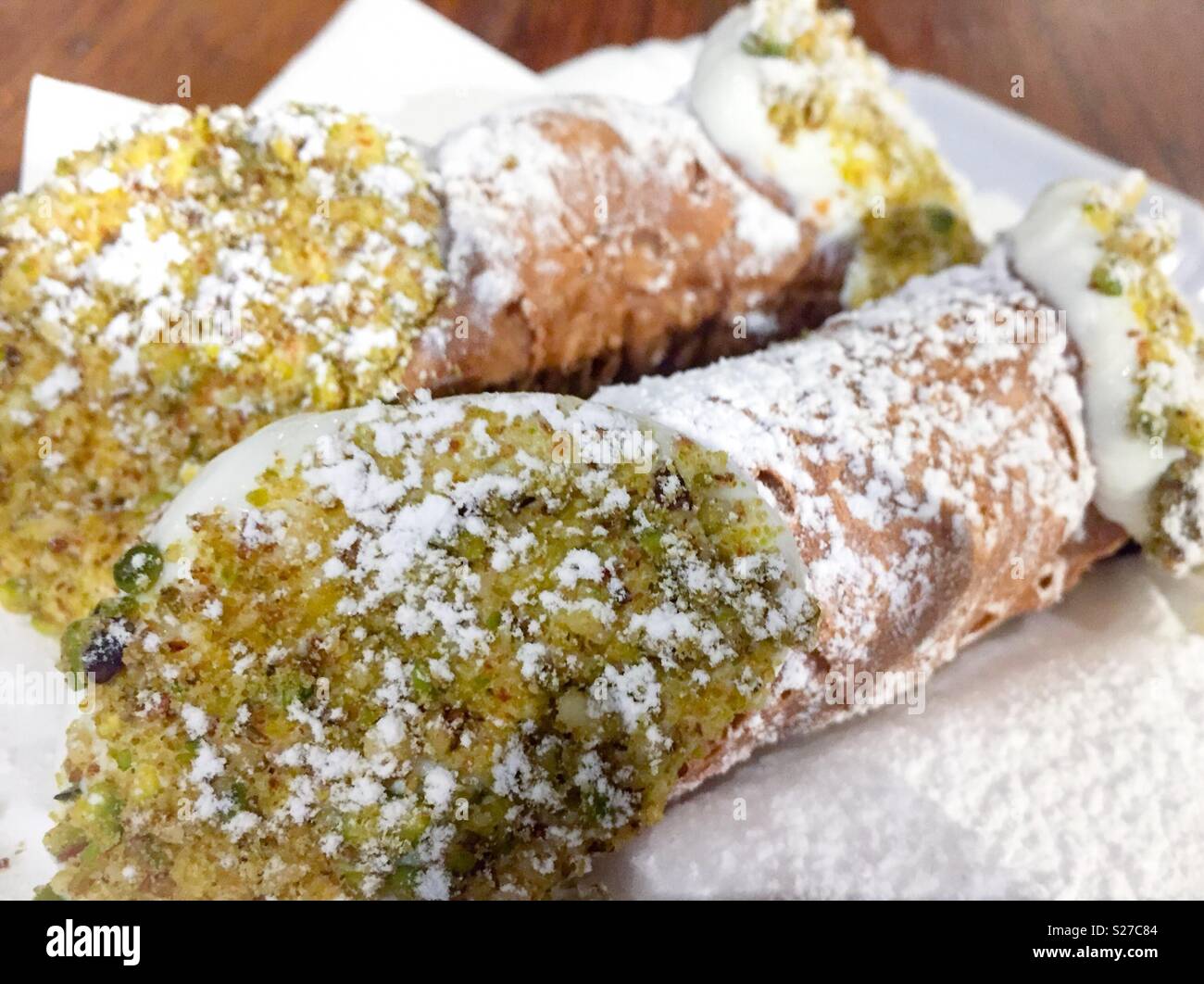 Cannoli- dessert italiano farcito con panna ricotta, immerso nei pistacchi tritati e spolverati con zucchero a velo. Foto Stock