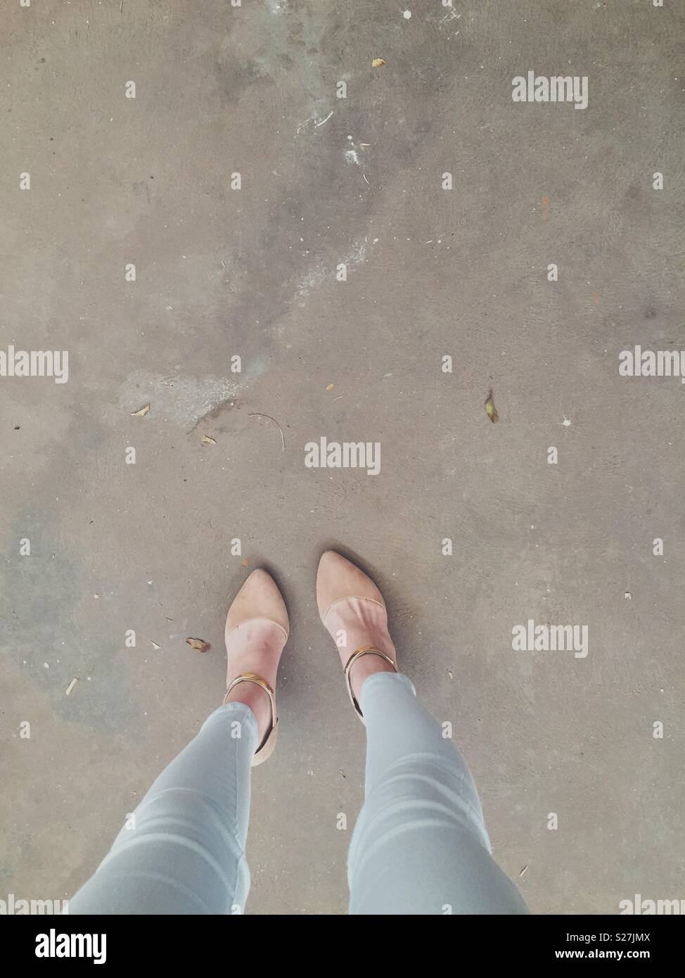 Tacchi e jeans in piedi su una pianura pavimento grigio Foto Stock