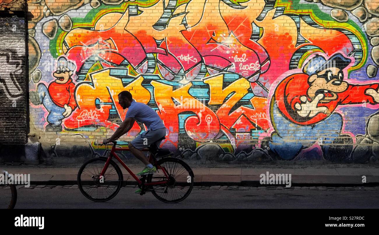 Un ciclista passa su una parete colorata di creative graffiti di Copenhagen, Danimarca. Credito foto - © COLIN HOSKINS. - Immagine stock catturata con smartphone