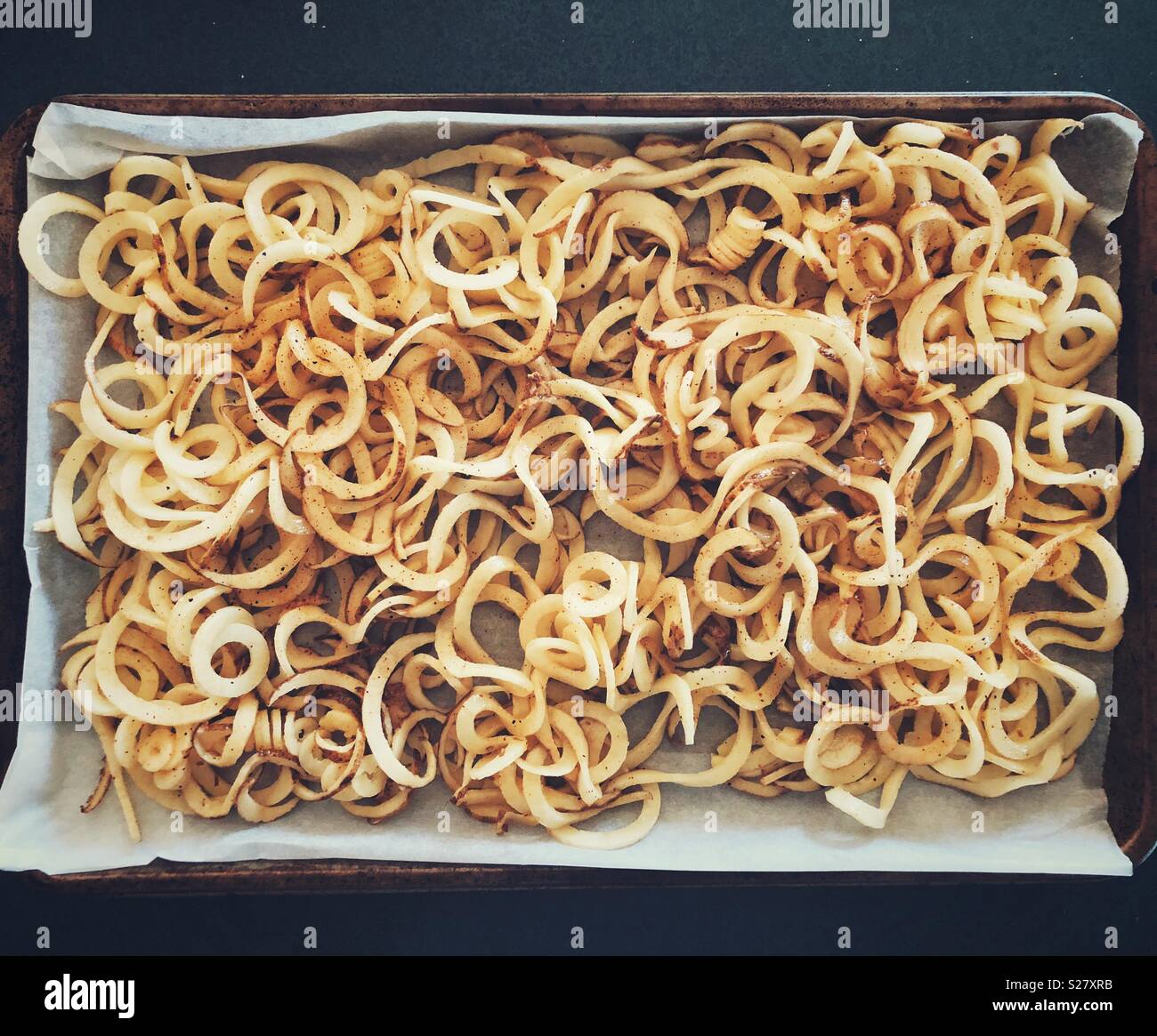 Fresche, materie spiralizzato patate bianche rivestite in olio d'oliva e stagionato su pergamena ricoperta di carta vassoio da forno Foto Stock