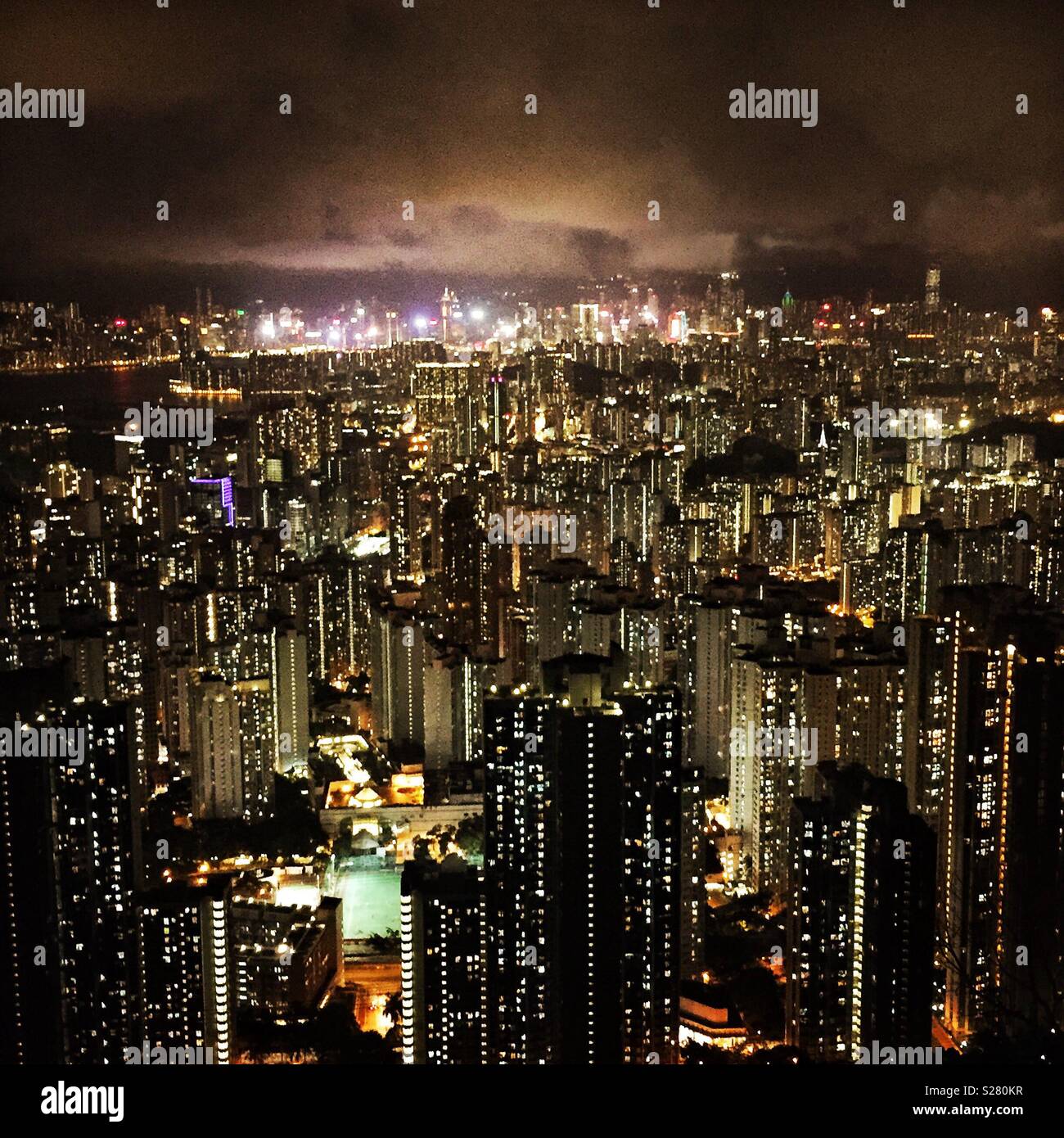 Le luci luminose dell'Isola di Hong Kong e Tsim Sha Tsui visto in tutta l'alta densità del paesaggio urbano della Penisola di Kowloon dal vecchio Sha Tin Pass Road, Hong Kong (tono caldo) Foto Stock